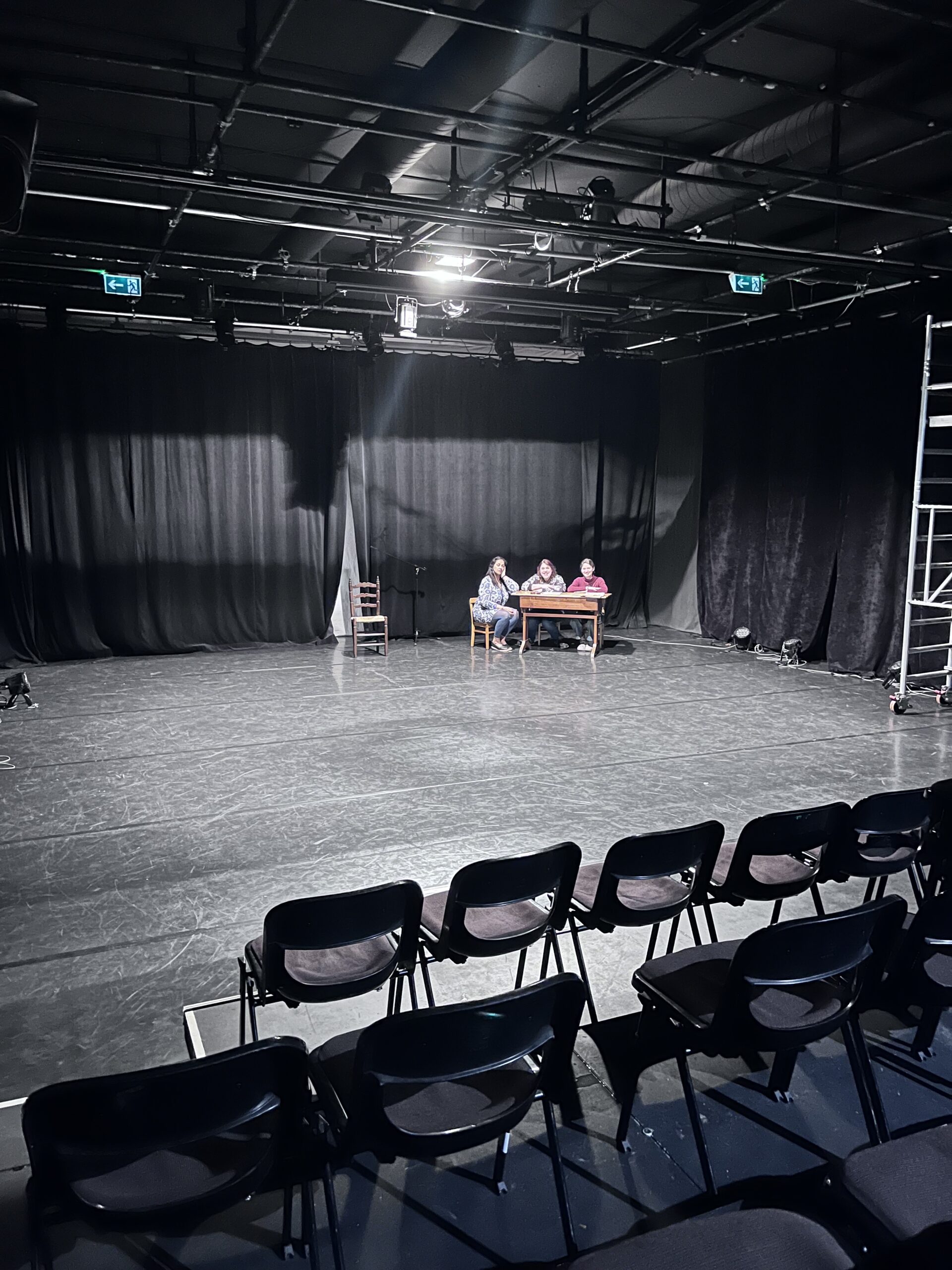 Trois interprètes autour d’une table sur le plateau du théâtre.