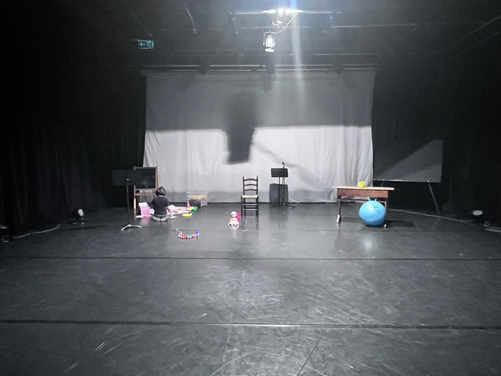 Une personne sur le plateau, parmi les objets d’enfance : chaises, tableau et ballon bleu.