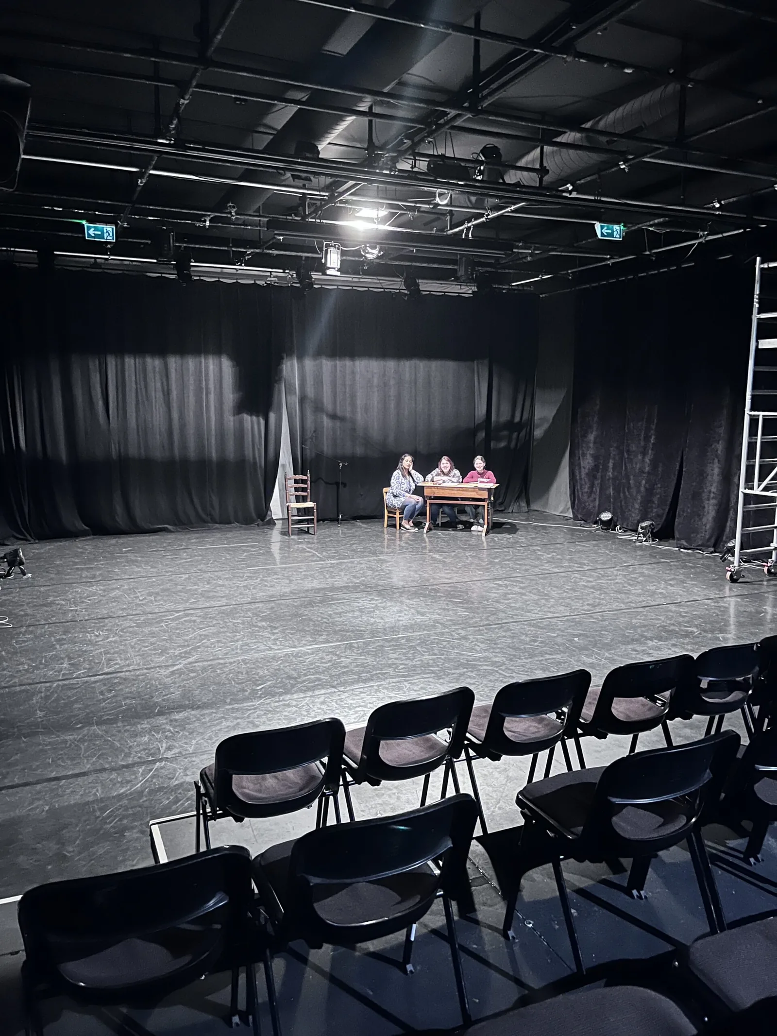 Trois interprètes autour d’une table sur le plateau du théâtre.