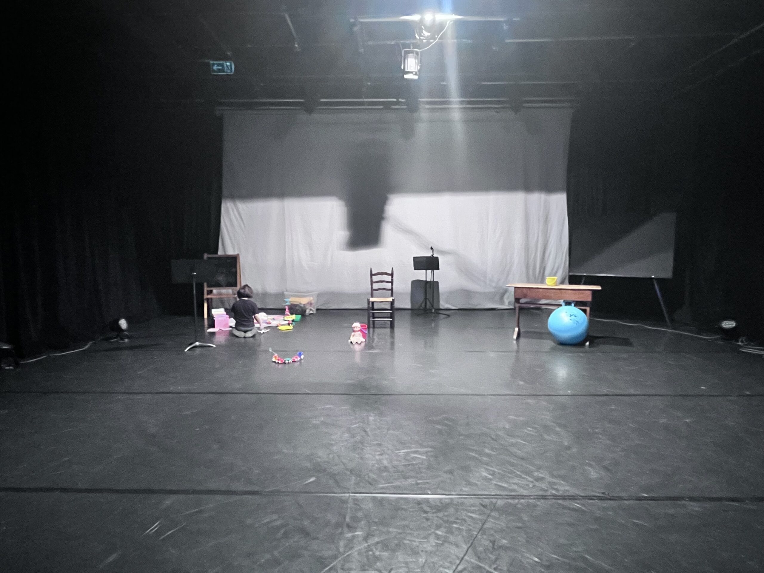 Une personne sur le plateau, parmi les objets d’enfance : chaises, tableau et ballon bleu.